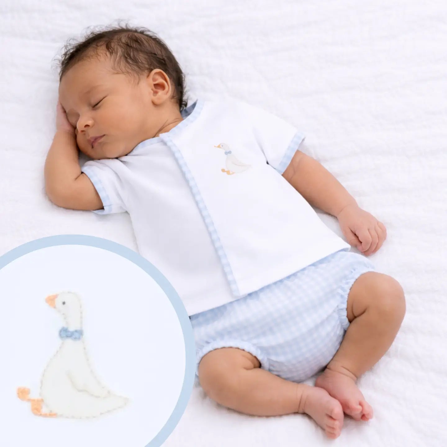 Baby sleeping in a white outfit with a blue pattern, surrounded by soft toys on a white background.