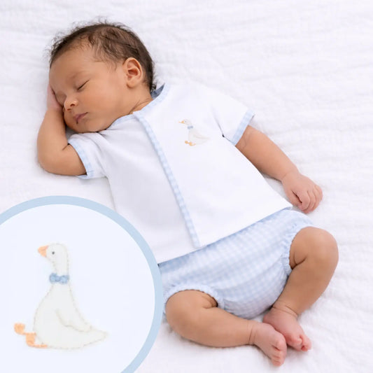 Baby sleeping in a white outfit with a blue pattern, surrounded by soft toys on a white background.