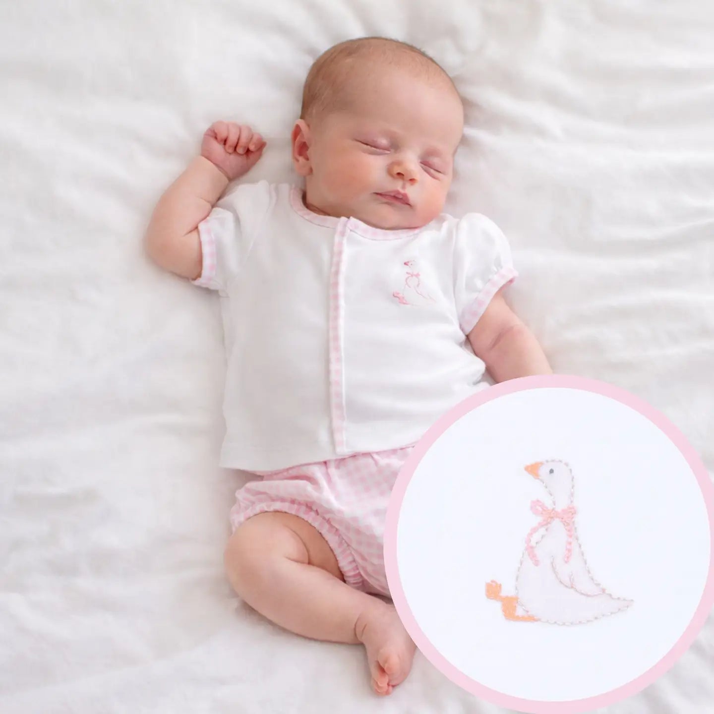 Newborn baby in a white outfit with a pink duck design, lying on a white blanket.