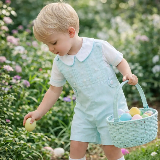 Child in light blue outfit with Easter eggs and basket outdoors