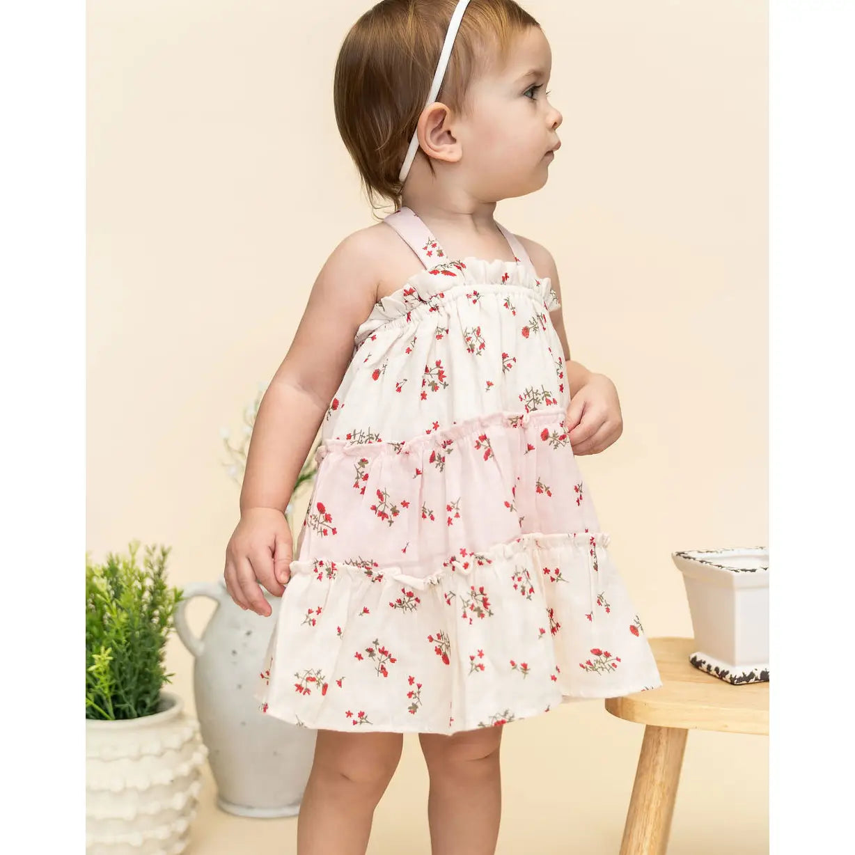 Baby girl wearing a floral dress standing in a room with decorative elements.