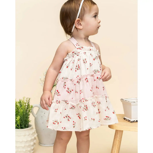 Baby girl wearing a floral dress standing in a room with decorative elements.
