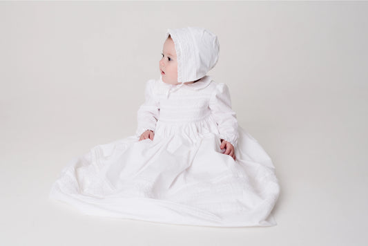 Baby in a white dress and headscarf on a light gray background