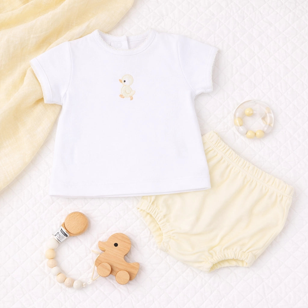 Baby outfit with white shirt, yellow shorts, and wooden toys on a light background